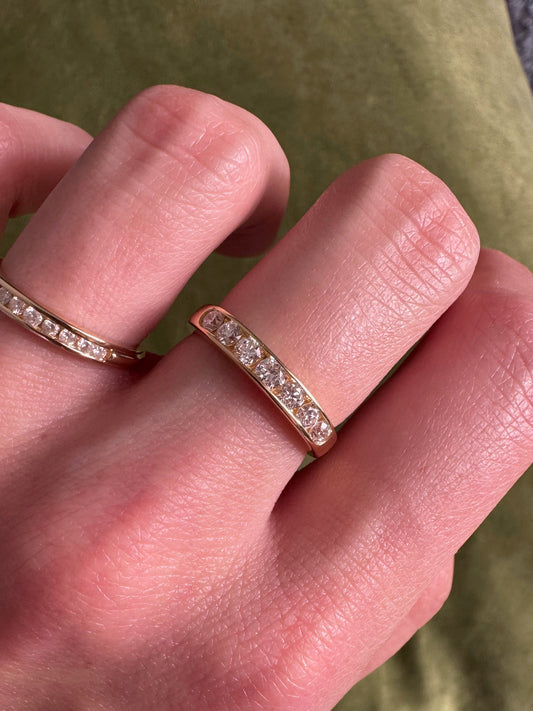 A close-up of a hand wearing two slim rose gold rings with pavé-set diamonds, resting against an olive green fabric background.